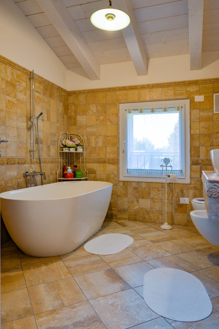 Bagno con vasca freestanding, rivestimenti chiari e finestra.