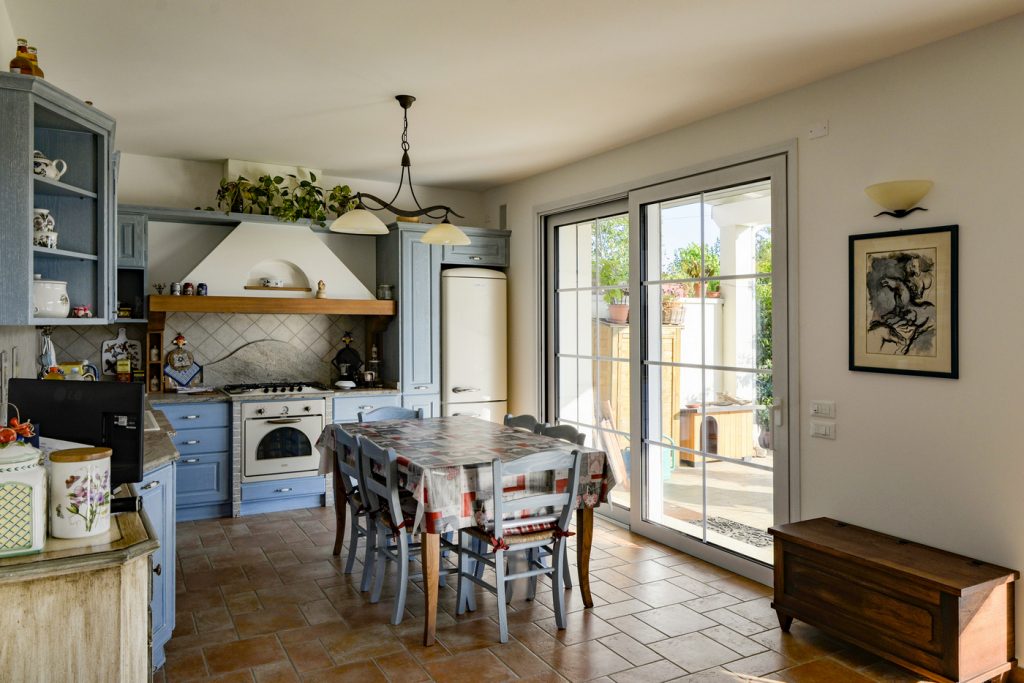 Cucina con arredi azzurri, tavolo da pranzo e portafinestra.