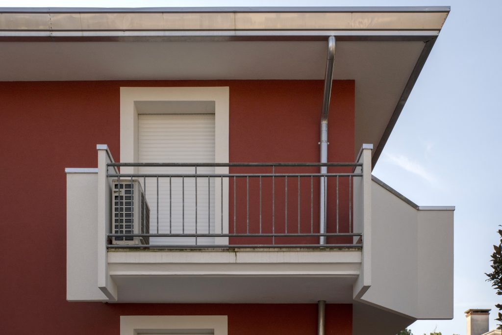 Balcone con parapetto metallico su una facciata color rosso mattone.